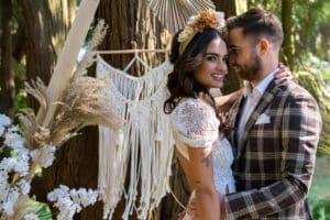 Brautpaar bei Boho Hochzeit vor Blumendekoration mit weissem Brautkleid und Blumen im Haar